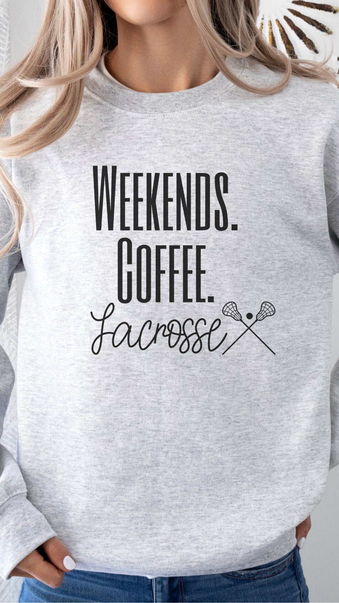 custom lacrosse sweatshirt for Moms that says weekends coffee lacrosse with a black outlined lacrosse sticks on the bottom. This sweatshirt comes in sand, white, black, gray, and heareth dark gray.