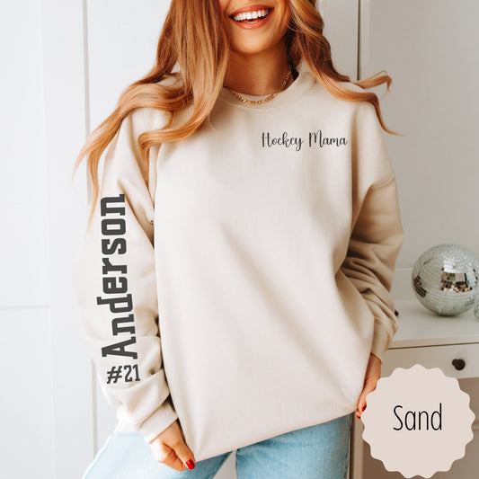 Custom hockey mom sweatshirt with name and number on sleeve. This shirt says hockey mama on the pocket area of the sweatshirt and the number with last name on the sleeve. This comes in sand, white, black, and ash gray.