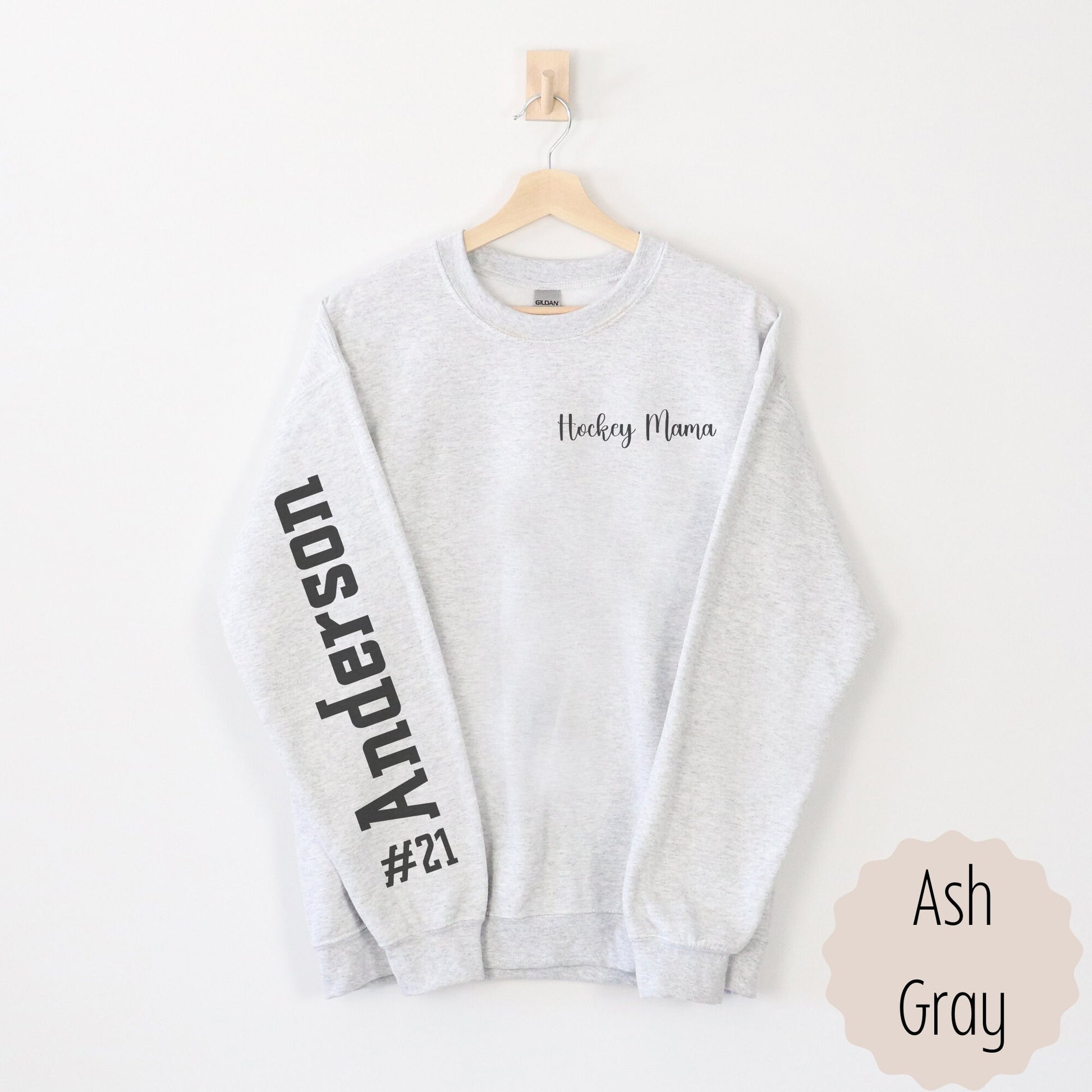 Hockey Game Day Sweatshirt with name and number on sleeve. This shirt says hockey mama on the pocket area of the sweatshirt and the number with last name on the sleeve. This comes in sand, white, black, and ash gray.